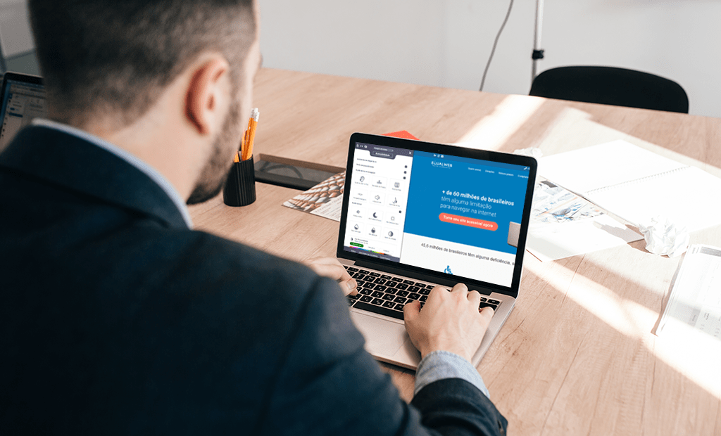 empresa. homem de costas, vestindo um paletó escuro, sentado à mesa enquanto usa um laptop. Na tela do laptop, o site da equalweb brasil está aberto.
