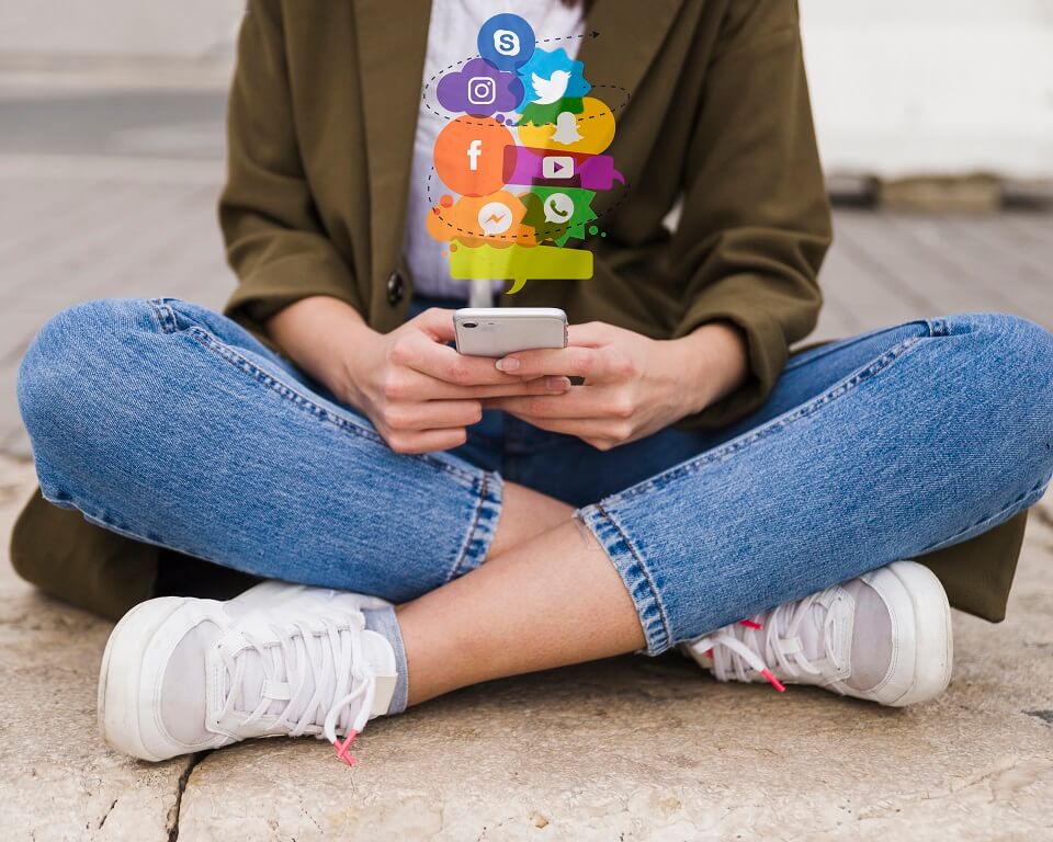 Pessoa com smartphone e ícones de redes sociais flutuando, simbolizando conectividade digital e acessibilidade nas plataformas.