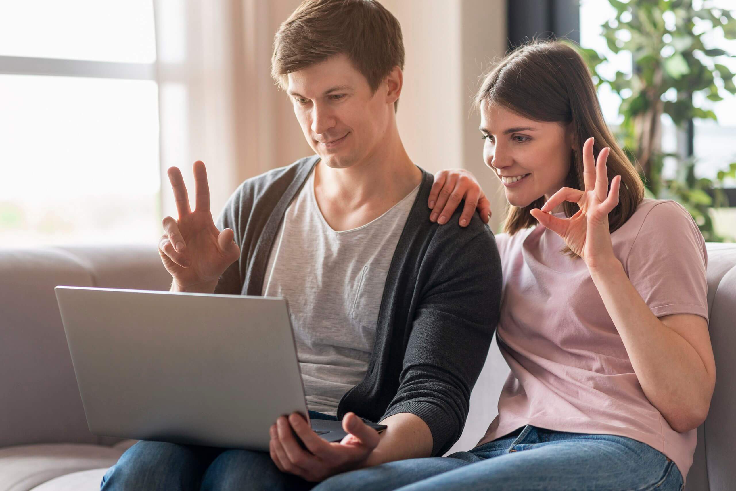 Casal usando laptop e fazendo sinal de OK com as mãos, ilustrando comunicação acessível e sucesso na interação digital.