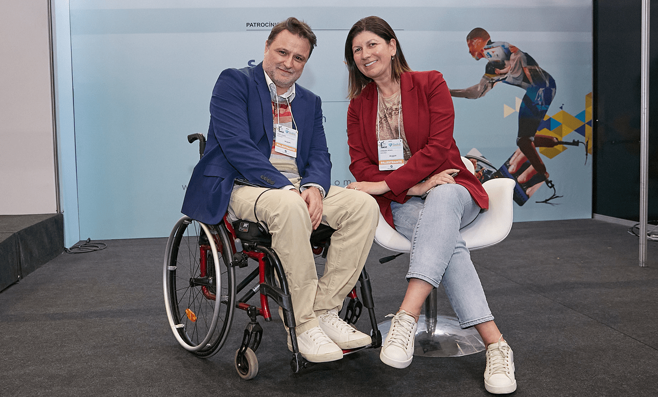 Homem em cadeira de rodas e mulher com crachá de palestrante posam juntos na Reatech 2022, evento da EqualWeb sobre acessibilidade digital.