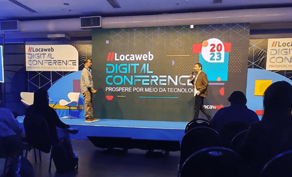 Dois homens palestram na Locaweb 2023 sobre tecnologia e acessibilidade digital para uma plateia atenta.