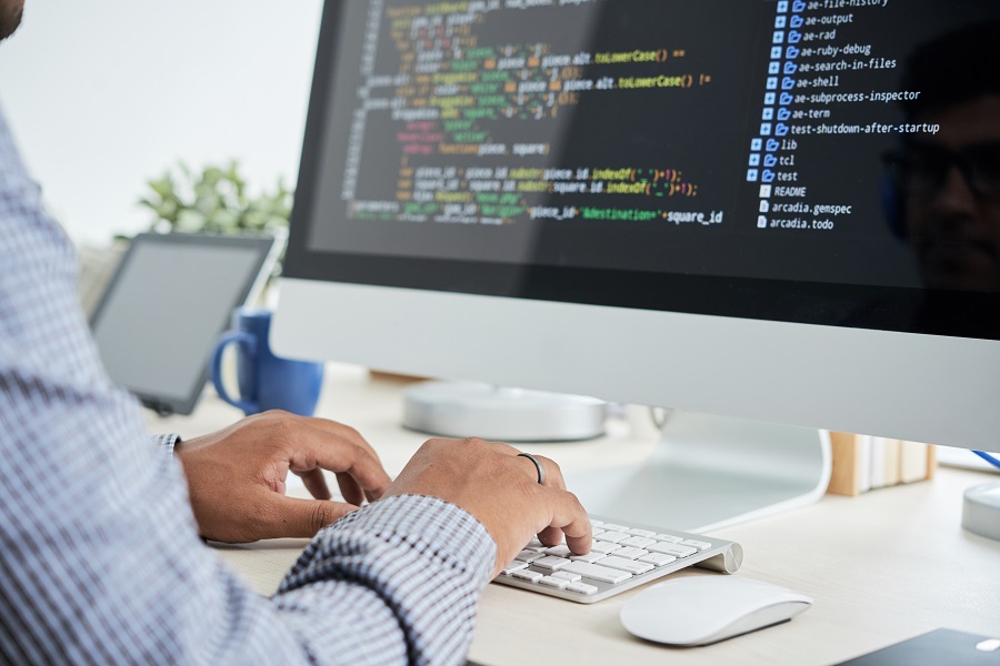 Mãos digitando em teclado diante de monitor com código, ilustrando desenvolvimento de software e novas diretrizes de acessibilidade web.