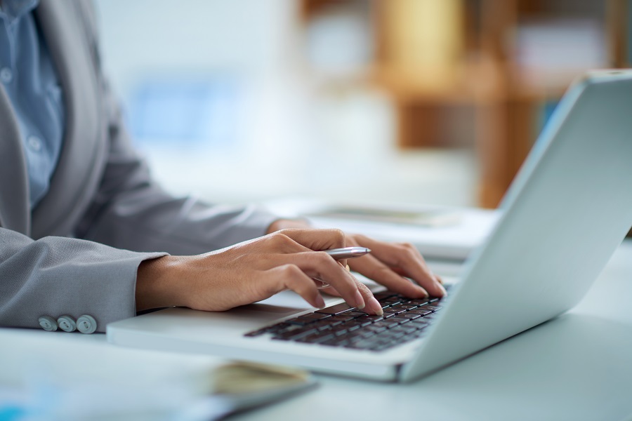 Mãos digitando em um laptop prateado, representando o uso diário da tecnologia e a importância de sites acessíveis para todos os usuários.