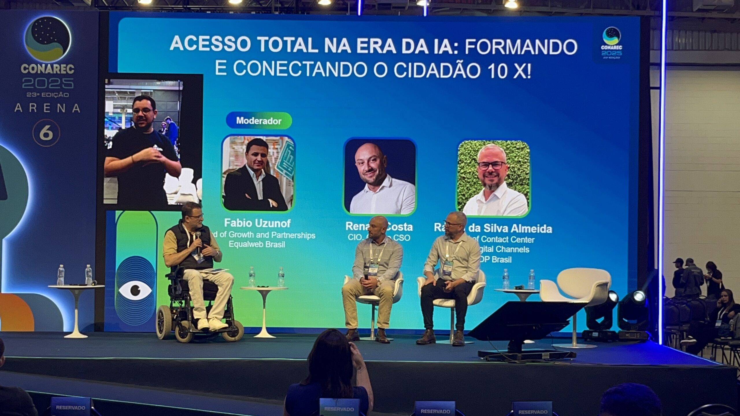 Painel CONAREC 2025: moderador cadeira de rodas e dois palestrantes. Tela mostra "Acesso Total na Era da IA" e nomes dos participantes.