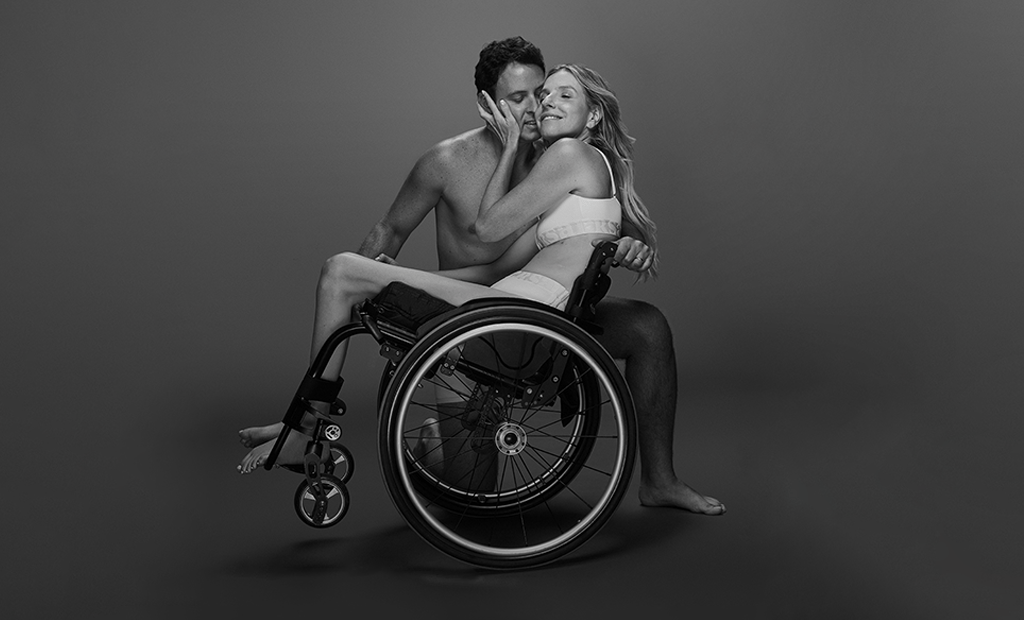 Casal em preto e branco: mulher em cadeira de rodas sentada no colo do parceiro, ilustrando representatividade e acessibilidade no amor.