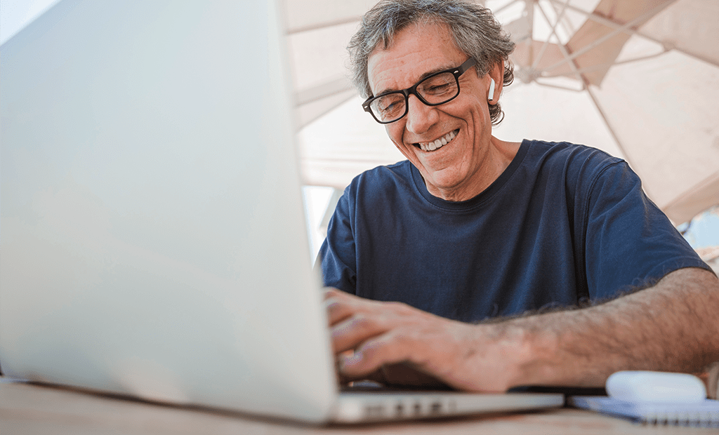 Homem sorridente usando laptop com óculos e fones, ilustrando acesso digital inclusivo e sua relação com SEO e desempenho online.
