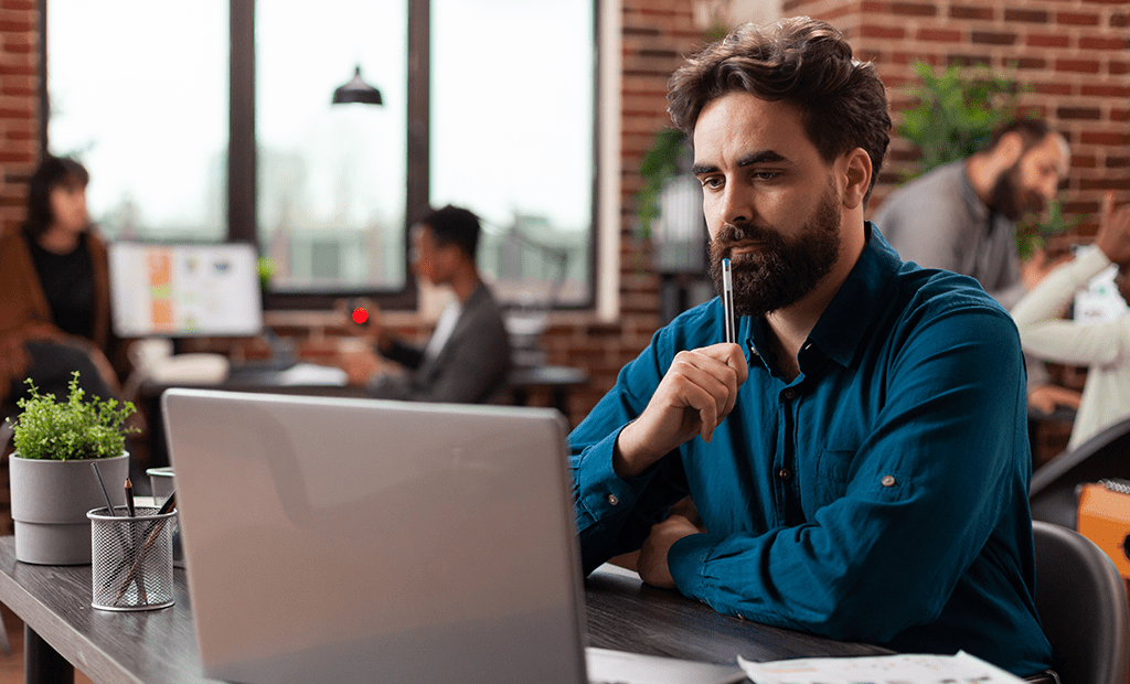 Homem concentrado em laptop no escritório, representando análise técnica e resolução de dúvidas sobre tecnologia acessível.