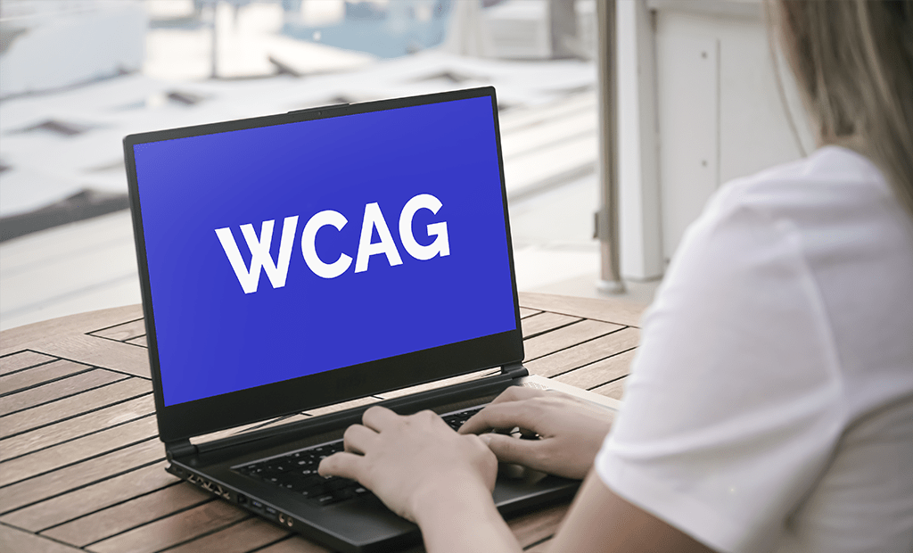 Pessoa digitando em laptop com tela azul exibindo "WCAG", representando diretrizes de acessibilidade web para conformidade com a LBI.