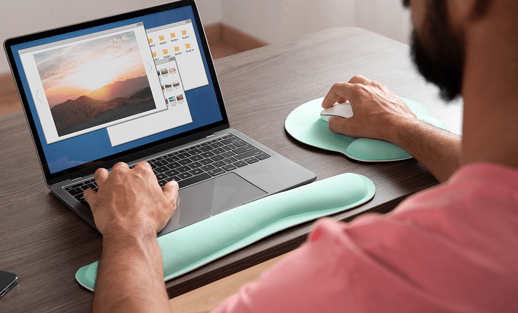 Pessoa usando laptop com protetores de pulso verde-água, navegando por imagens em uma pasta no ecrã.