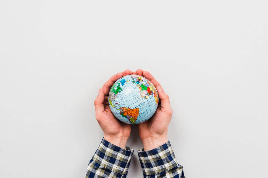 Mãos segurando um pequeno globo terrestre sobre fundo branco, simbolizando responsabilidade global e cuidado com o mundo.