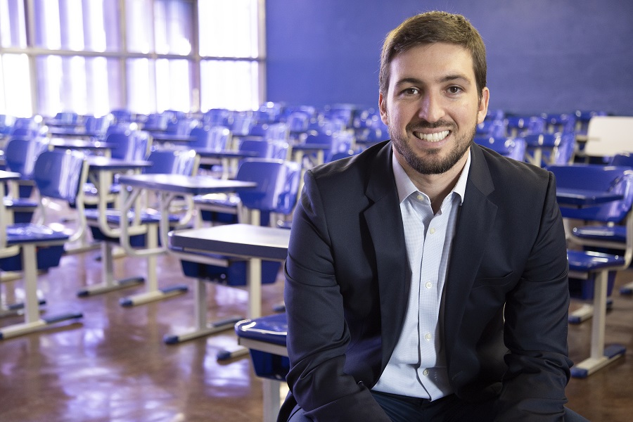 Homem de terno sorrindo em sala de aula com carteiras azuis, representando o caso UNISUAM e a acessibilidade web com EqualWeb.