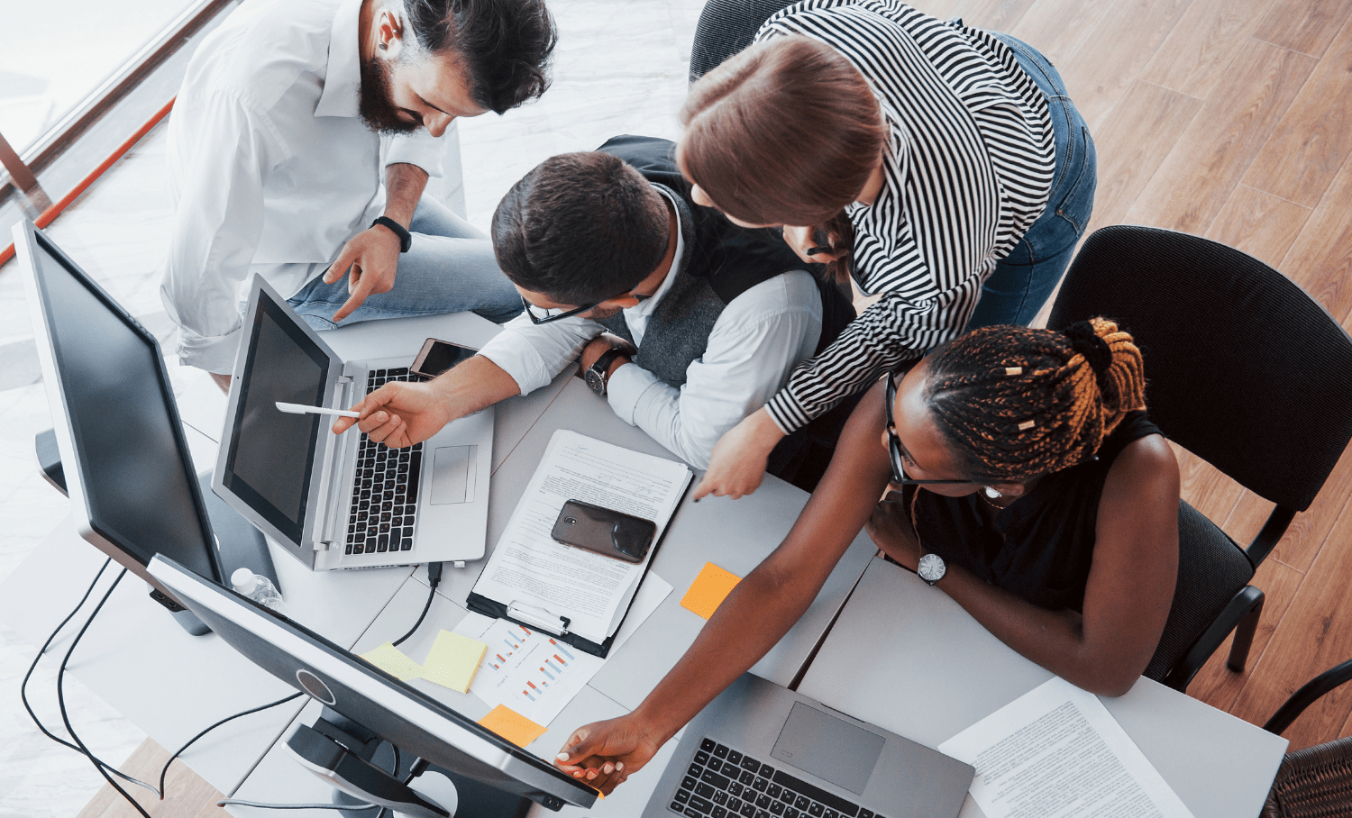 Equipe diversa colabora com laptops e gráficos, ilustrando trabalho em equipe e inclusão no ambiente corporativo.