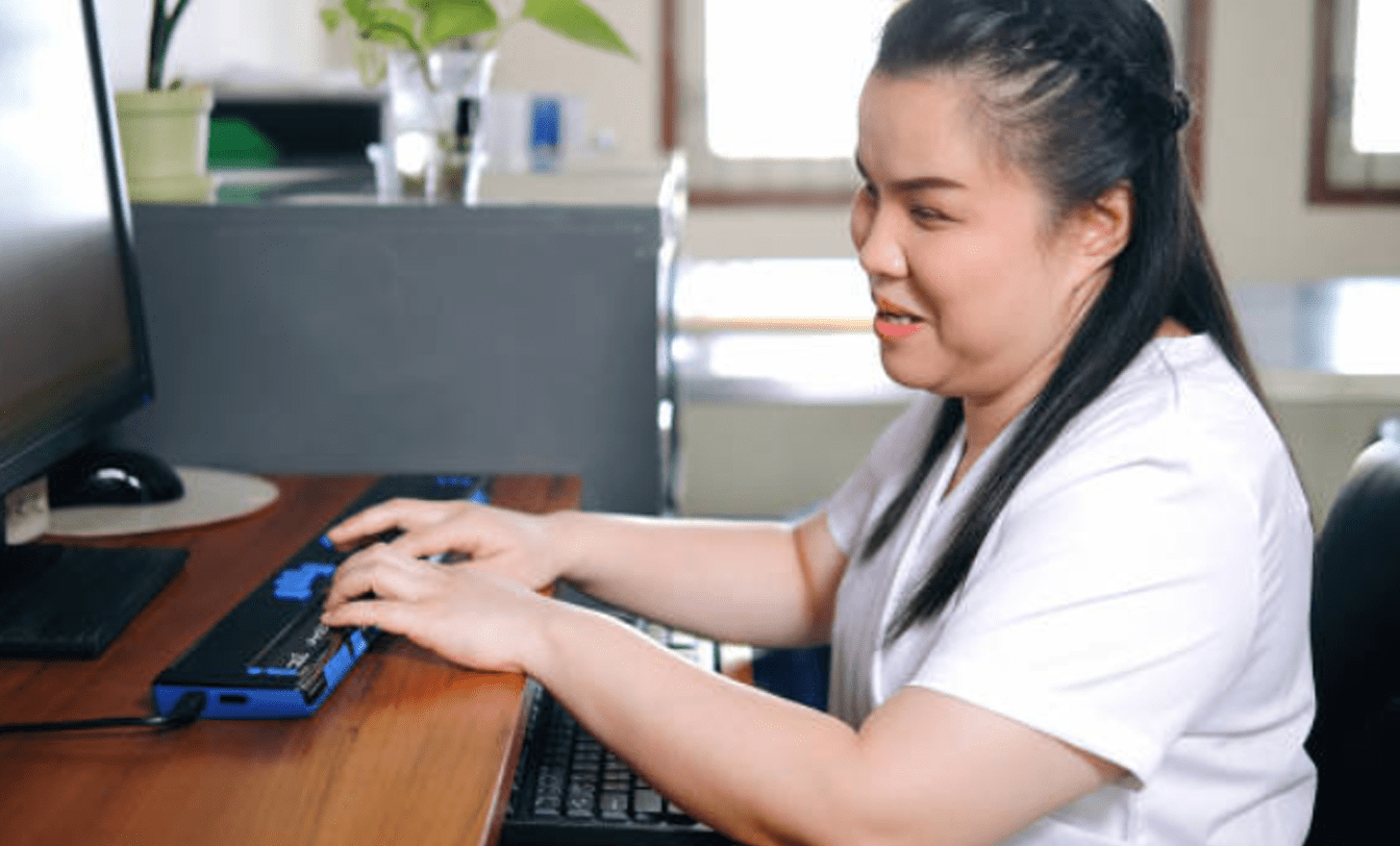 Pessoa digita em teclado azul adaptado sobre mesa de madeira, demonstrando tecnologias assistivas para acessibilidade e inclusão digital.