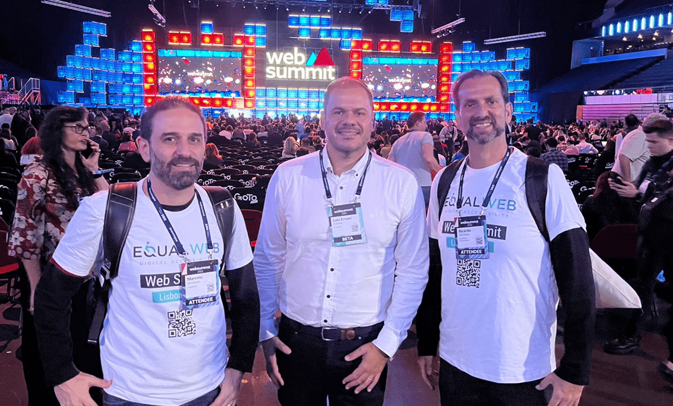Três homens, dois com camisas EqualWeb, posam no Web Summit 2022 em Lisboa. Ao fundo, palco iluminado com logo e plateia lotada.