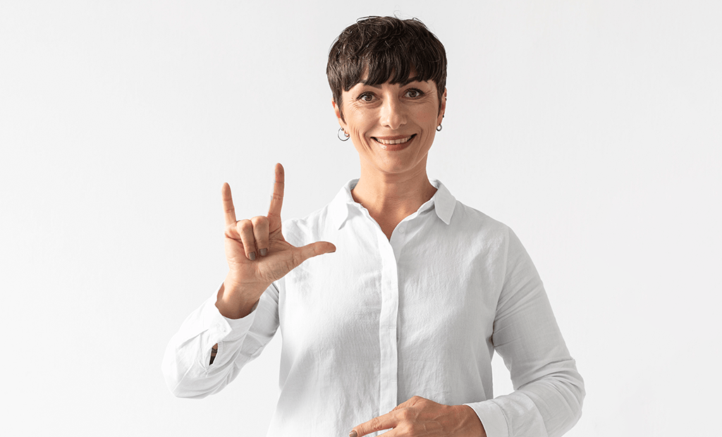 Mulher usando Libras com gesto de "L" e polegar estendido, simbolizando comunicação acessível e inclusão digital para a comunidade surda.