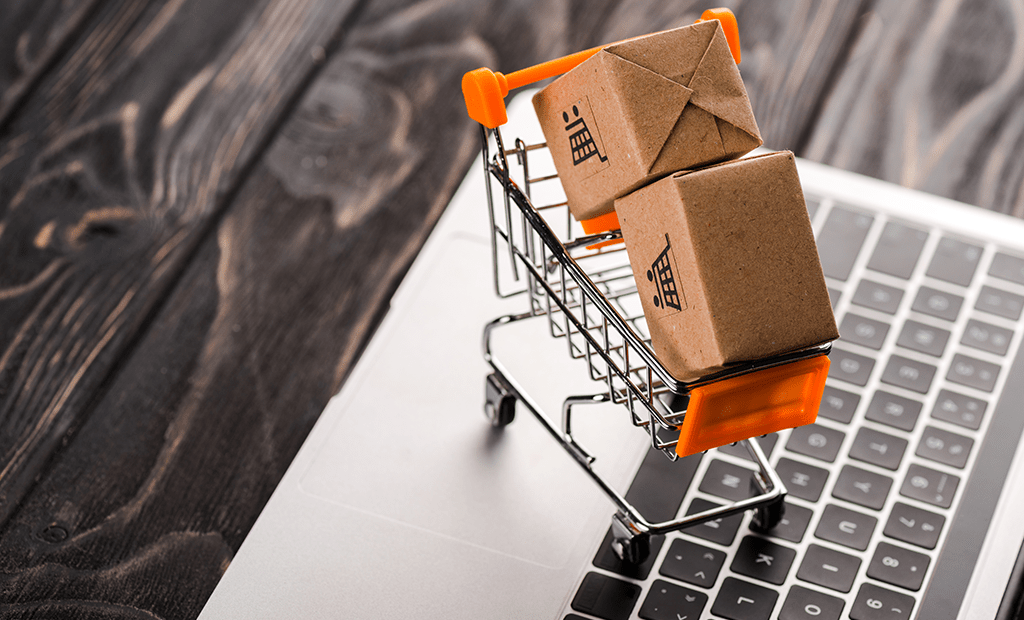 Carrinho de compras miniatura com pacotes sobre teclado de laptop, simbolizando e-commerce e vendas online para datas comerciais.