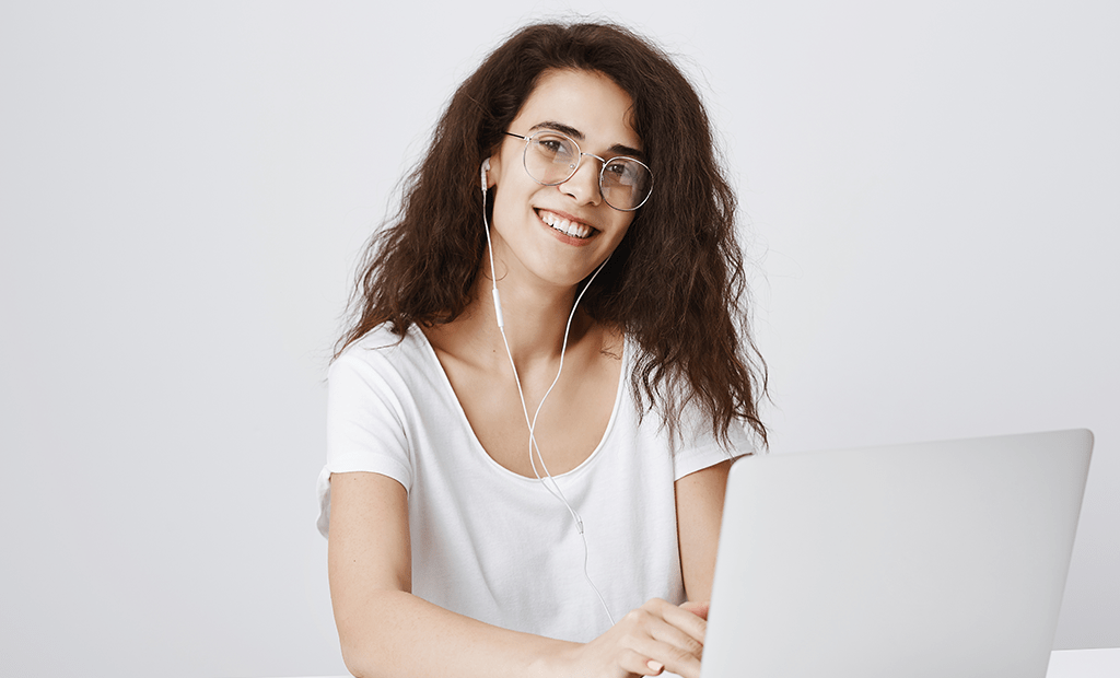 Mulher sorridente com óculos e fones de ouvido usando laptop, representando acesso digital inclusivo e experiência do usuário acessível.