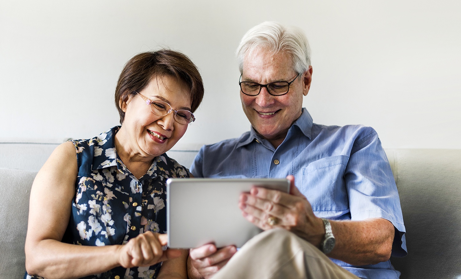 Idosos usam tablet no sofá, ilustrando tecnologia e acessibilidade digital para a terceira idade.