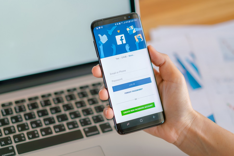 Smartphone exibindo tela de login do Facebook, com campos para e-mail e senha, botão azul "LOG IN" e opção verde para criar nova conta.