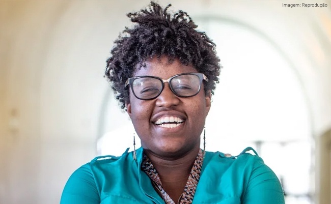 Mulher negra de óculos e camisa verde sorri. Imagem ilustra a IA como aliada na inclusão digital.