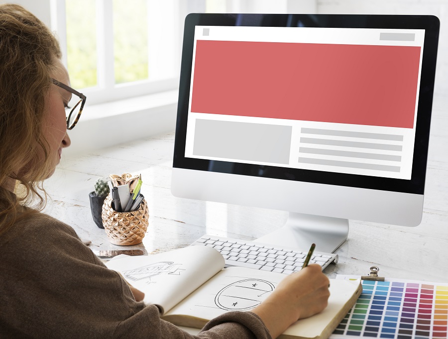 Profissional desenha layout em caderno com wireframe na tela, ilustrando o processo de planejamento e testes de acessibilidade web.