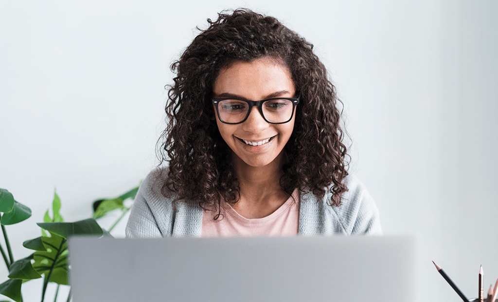 Afya. Imagem de uma menina negra de cabelos cacheados, usando óculos. Ela digita em um notebook.
