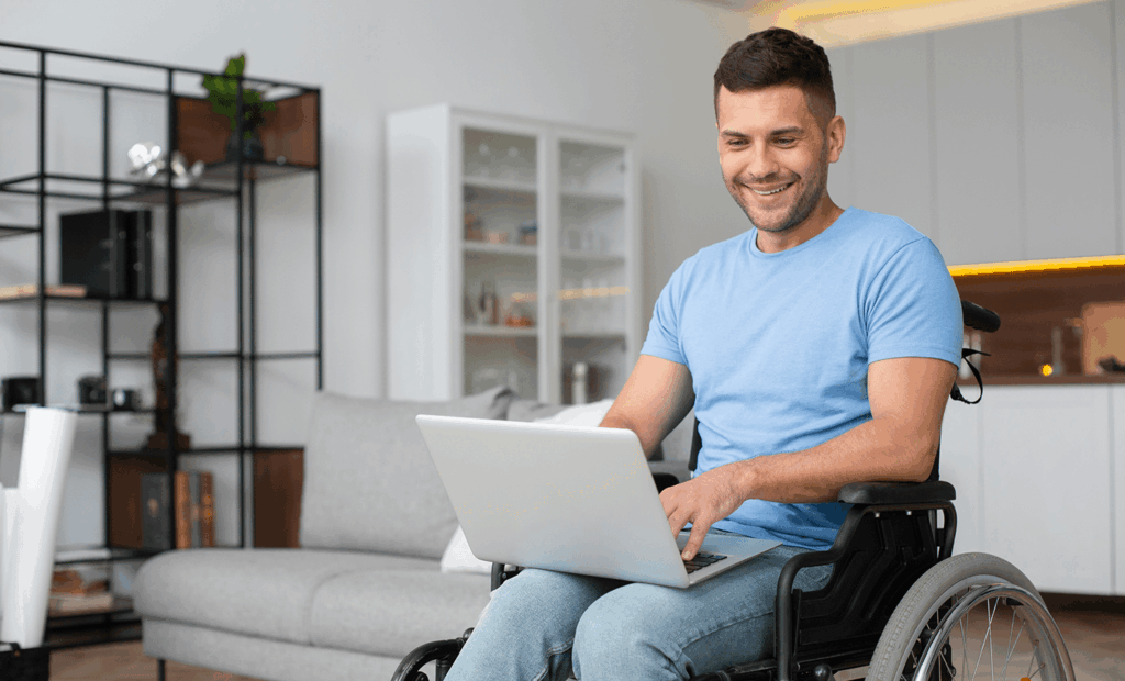 saúde. Imagem de um homem branco e de cabelos escuros, cadeirante em uma sala mexendo no notebook.