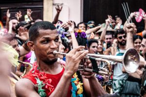 Na foto temos um rapaz tocando trompete em um bloco de rua no carnaval
