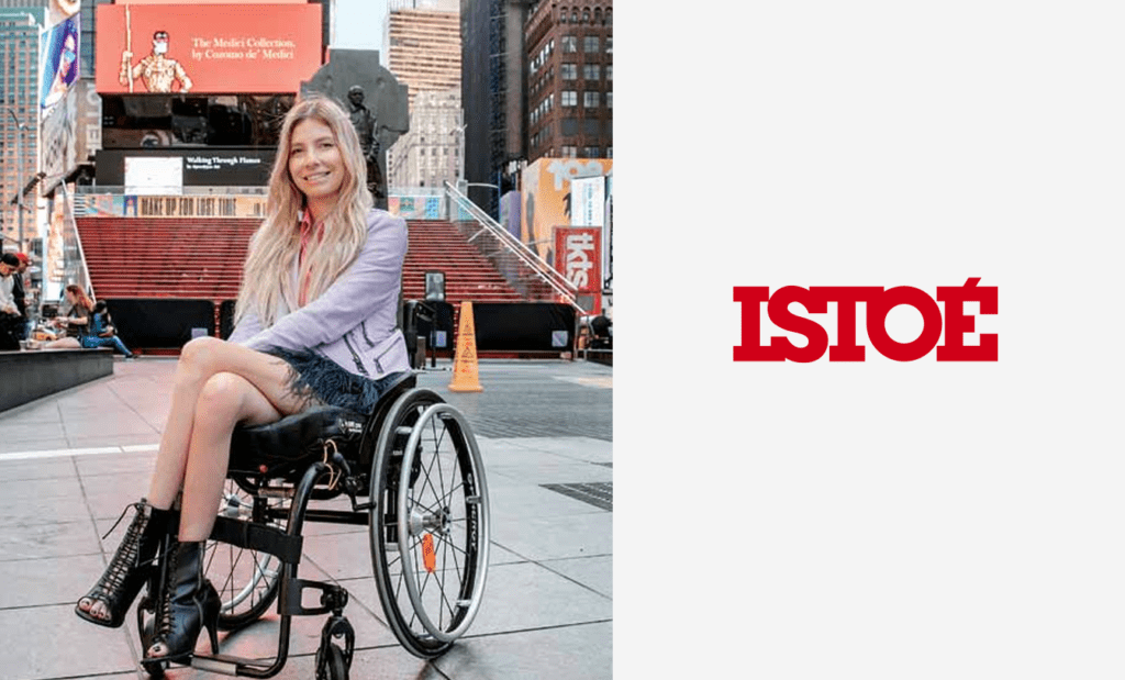 PCD. Uma imagem dividida em duas: Do lado esquerdo temos a foto de Andrea Schawarz sentada na sua cadeira de rodas de saia, blazer e sapatos pretos em frente a um prédio na Times Square. Do lado direito temos em vermelho a logo da isto é.