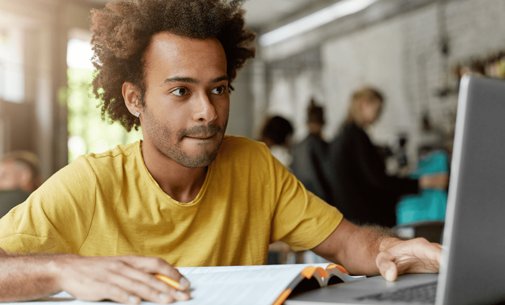 educação. Menino negro de camisa amarela estudando com um livro e um notebook.