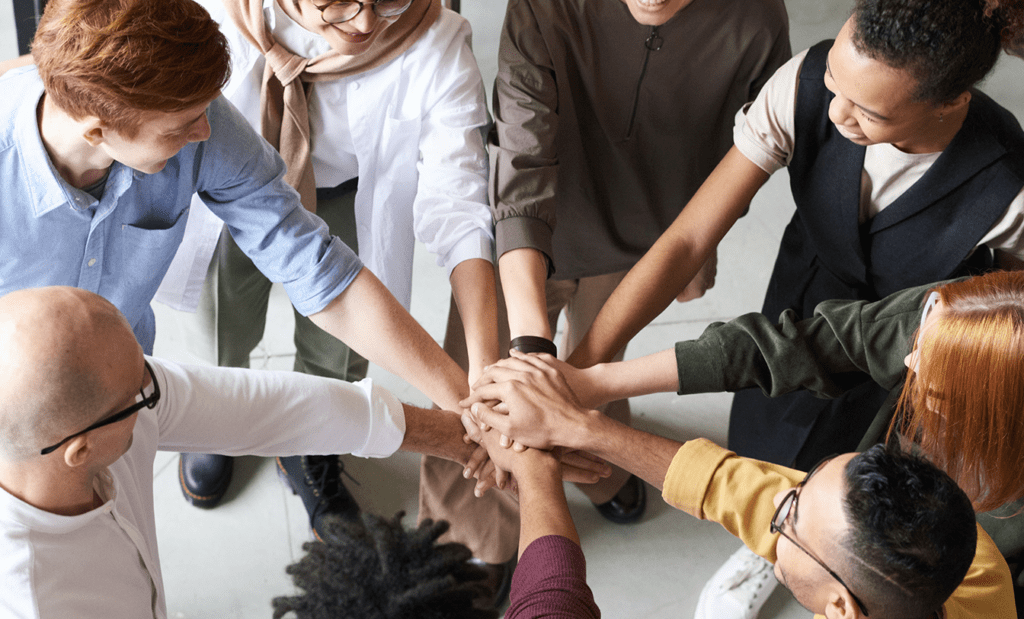 futuro. Imagem de um grupo de pessoas com as mãos postas uma sobre as outras, formando elo de união. Na imagem temos, pessoas brancas, pardas e negras.