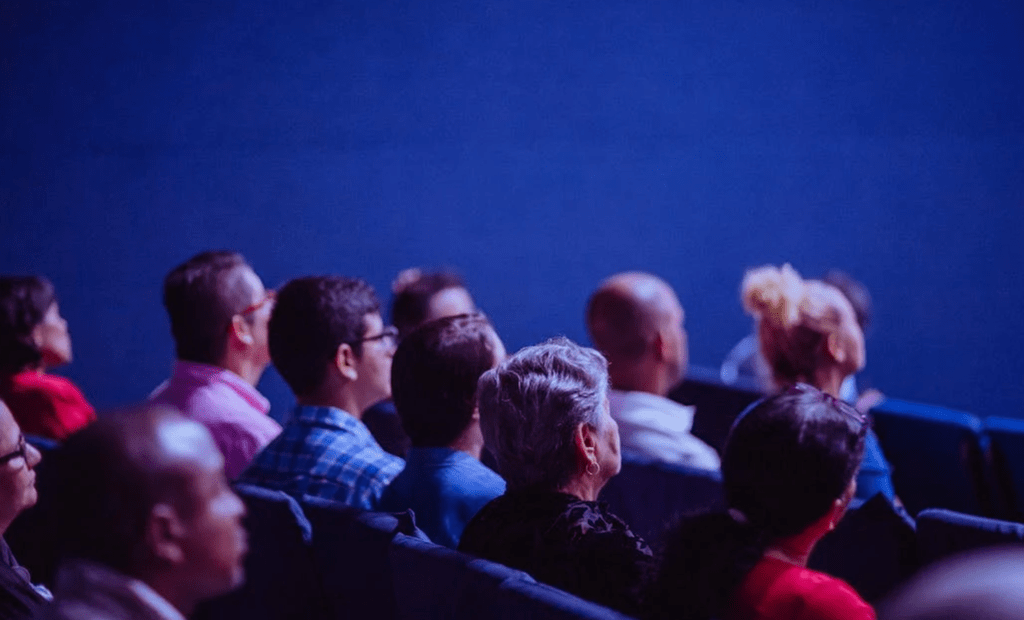 entretenimento. Imagem de uma sala de cinema e algumas pessoas assistindo o filme. 