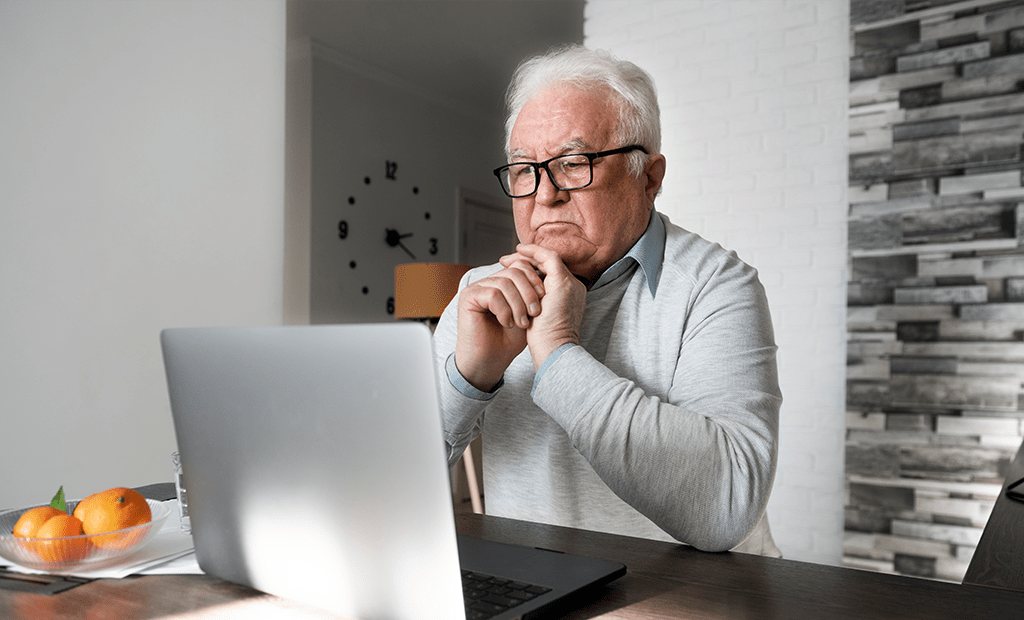 Acessibilidade. Imagem de um idoso sentado na frente do notebook com uma feição pensativa.