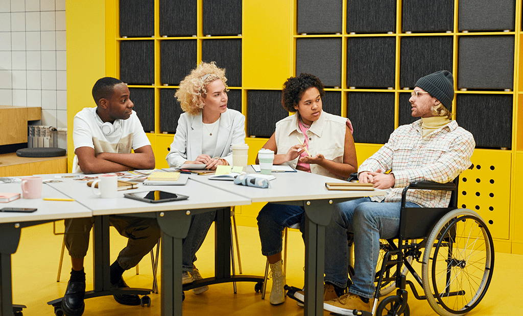 DEIA. Imagem de uma sala de reunião com algumas pessoas conversando em uma sala de reunião. Com as paredes preta e amarela.