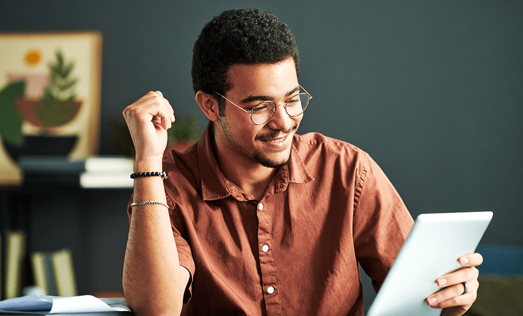  Epilepsia. Imagem de um homem negro usando óculos, blusa marrom e algumas pulseiras no braço. Ele está sorrindo enquanto olha para um tablet.