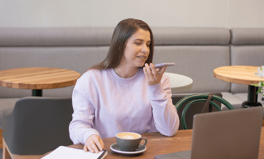IA. Imagem de uma mulher branca, usando moletom, cabelos longos falando ao telefone e tomando café.