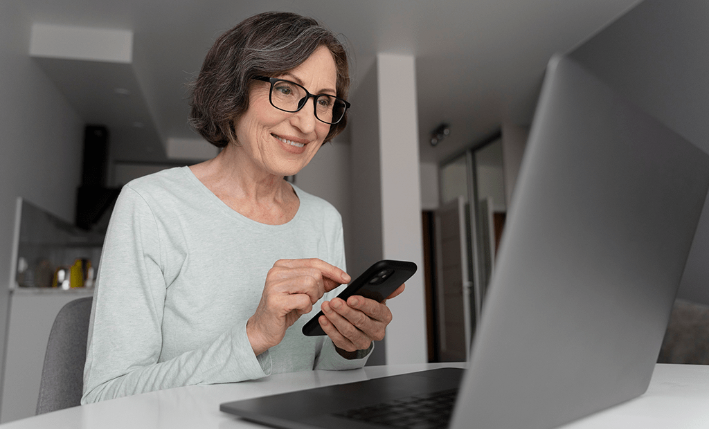 Dia do Cliente. Imagem de uma mulher aparentando mais de 50 anos mexendo no celular e usando um notebook.