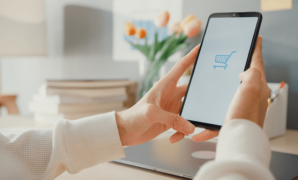 Dia do Cliente. Imagem de uma mão feminina segurando um celular e na tela dele aparece um carrinho de e-commerce;