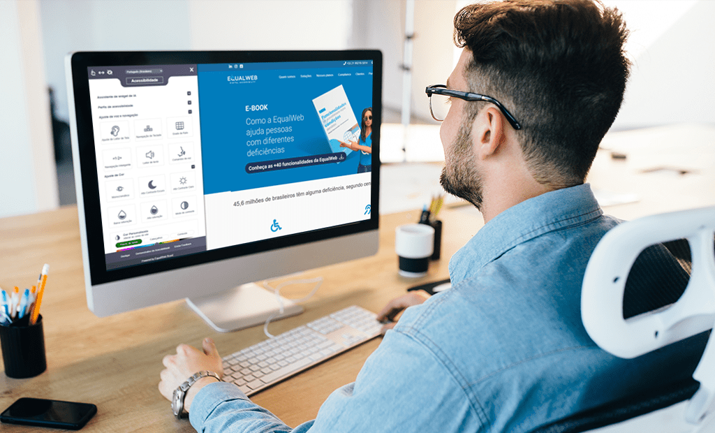 Empresas. homem de costas, sentado em uma cadeira de escritório branca com apoio para a cabeça, usando óculos e uma camisa azul. Ele está trabalhando em um computador de mesa (iMac) com um teclado e um mouse sobre uma mesa de madeira clara. A tela do computador exibe o site da equalweb.