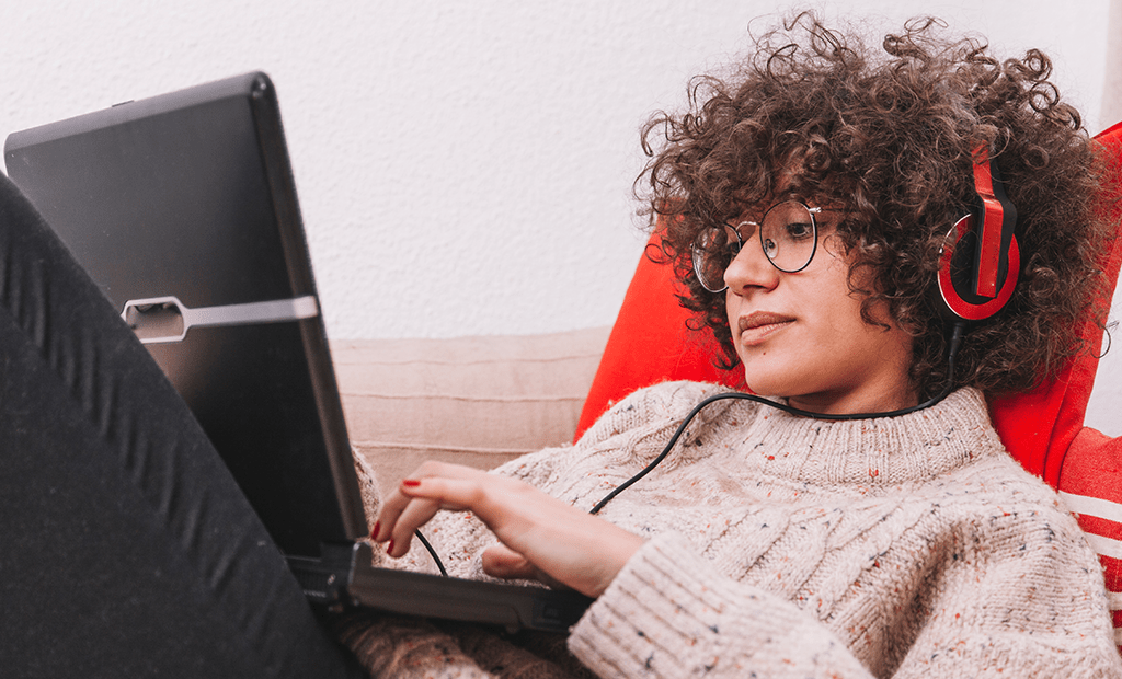 Leitores de tela. Pessoa com fones de ouvido e óculos usa notebook no colo enquanto está sentada no sofá.