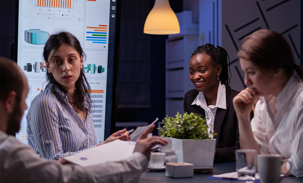 ROI da acessibilidade. Equipe diversa reunida à noite em sala de reunião moderna analisando gráficos em uma tela digital.