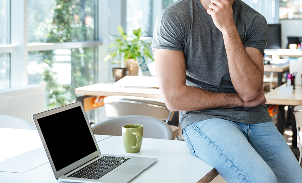 ROI da acessibilidade. Homem pensativo sentado em mesa de escritório moderno com notebook e caneca ao lado.