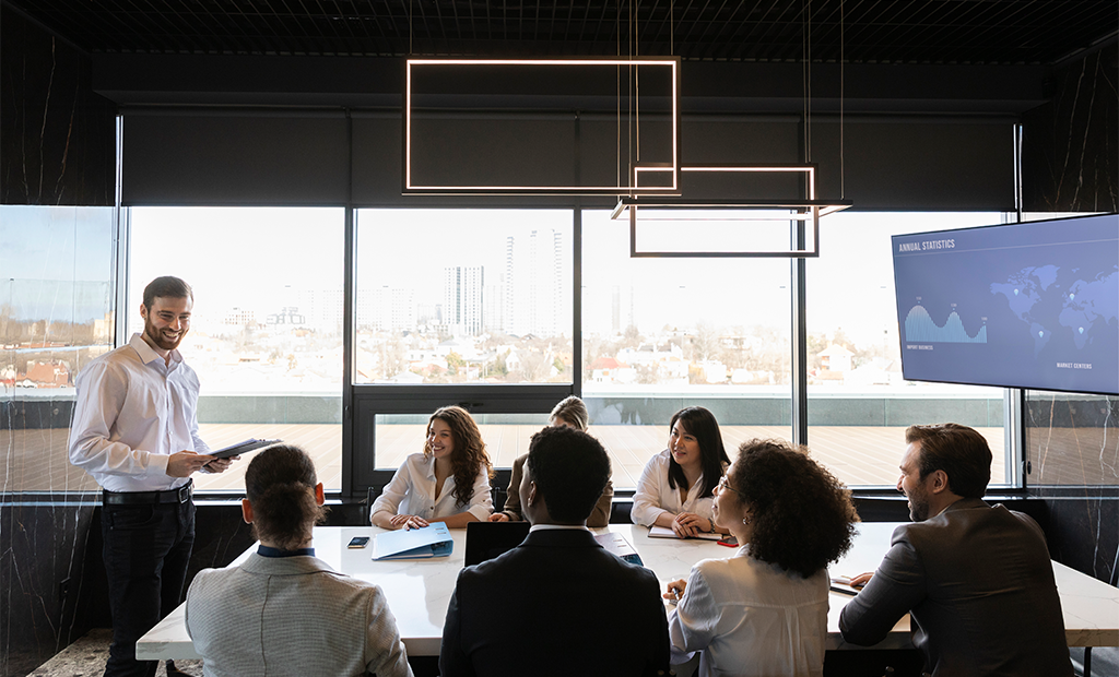 Acessibilidade digital. Homem apresenta dados para grupo em reunião de negócios, com tela de estatísticas e vista urbana ao fundo.